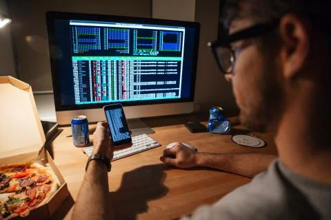 Serious developer in glasses using computer and smartphone Foto stock