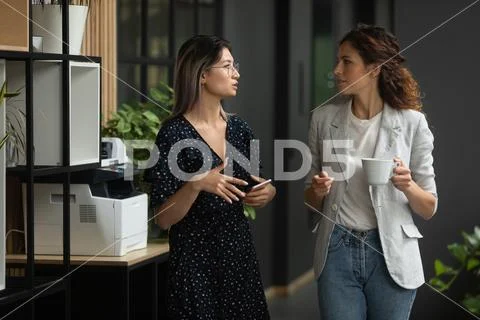 Serious diverse female colleagues talking walking in office space Stock Photos