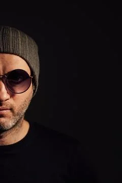 Serious dramatic man in sunglasses looking away while standing against black Stock Photos