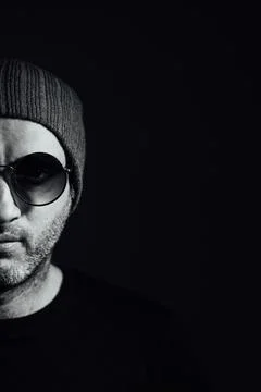 Serious dramatic man in sunglasses looking away while standing against black Stock Photos