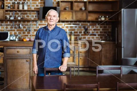 Serious elderly man standing in the kitchen Stock Photos