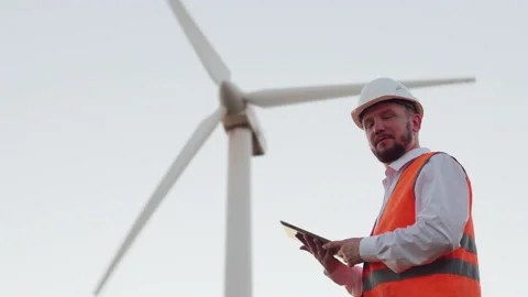 A serious engineer with a beard in an orange vest and hard hat looks at a modern Stock Footage 136030501
