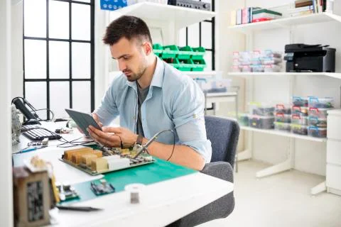 Serious engineer using tablet computer while working at table in electronics 스톡 사진