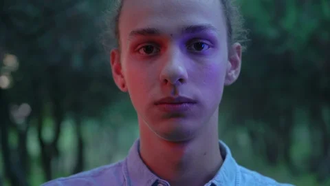 Serious face of young man lighted by red and blue light in the dark forest Video stock 96119713