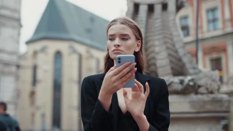Serious face young woman stand use phone near fountain in old street city social Stock Footage 139603353