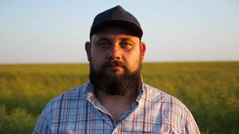 Serious farmer in cap looks into camera standing at cultivated field. Portrait Vídeos de archivo 252741730