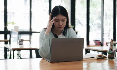 Serious focused Asian student using laptop in kitchen, looking at screen with Foto stock