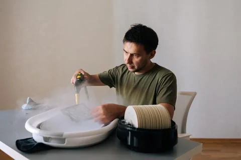 Serious focused young man using steam cleaner to clean air humidifier filter in Stock Photos