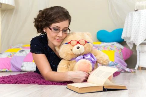 Serious girl and teddy bear reading a book in glasses Stock Photos