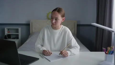 Serious girl using laptop while studying at table in bedroom at home Stock Footage 292728975