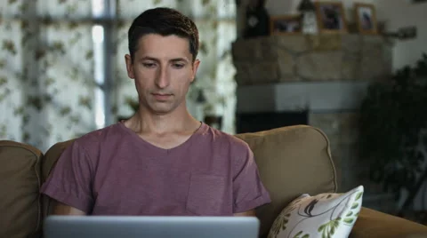 Serious good looking man working on his laptop while sitting on a couch in the Stock Footage 65990353