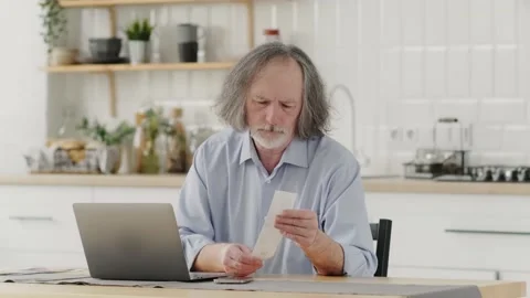 Serious grey-haired single aged senior man sitting at the table Living room with Stock Footage 237695849