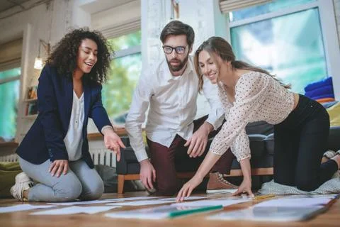 Serious guy and two smiling girls bent over papers Stock Photos