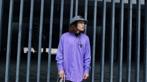 Serious guy posing near stadium gate. Hipster staying with skateboard outdoor. Stock Footage 158148491