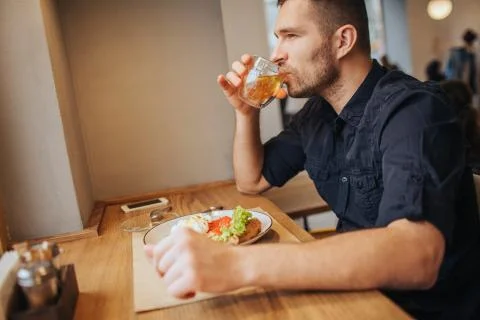 Serious guy is sitting at table and drinking tea. He is looking straight forw Foto stock