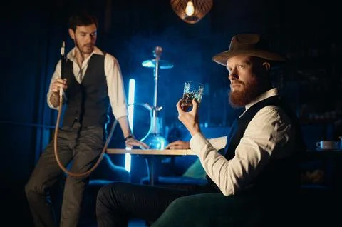 Serious guys smoking hookah while rest in pub Stock Photos