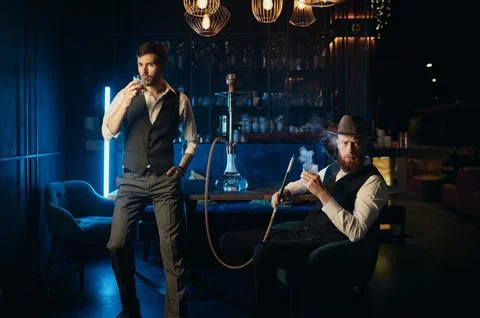 Serious guys smoking hookah while rest in pub Stock Photos