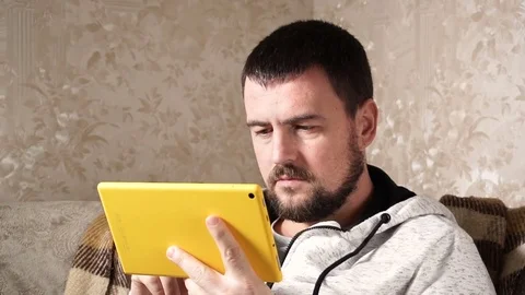 Serious handsome young man is using a tablet computer on couch at home. Stock Footage 83584878