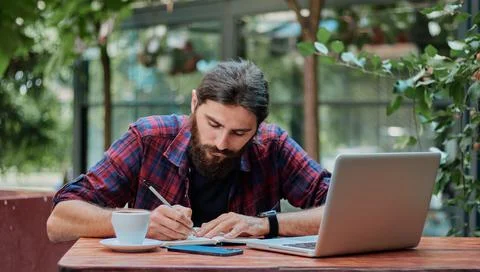 Serious hipster guy taking down notes in his notebook in a cafe. Foto stock
