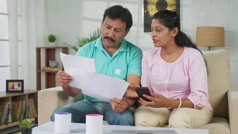 Serious indian couple checking bills or documents by using mobile phone while Stock Footage 247777661