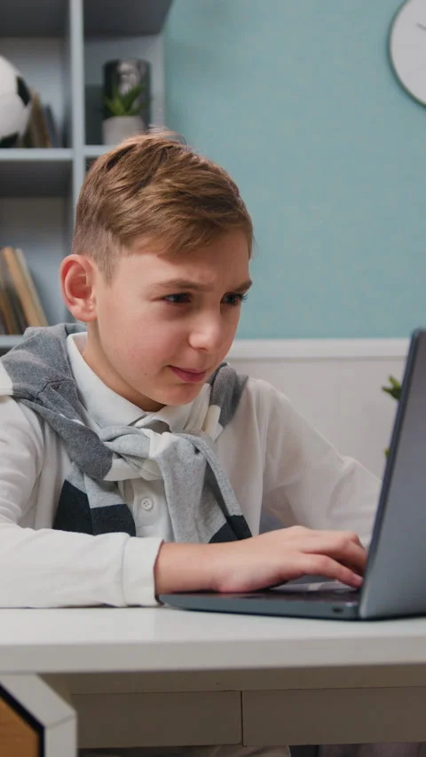 Serious kid working with laptop computer sitting at desk at home. Boy home, chil Stock Footage 329884836