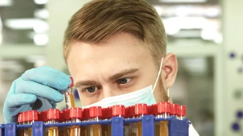 A serious lab technician studies test tubes with assays Stock Footage 84862482