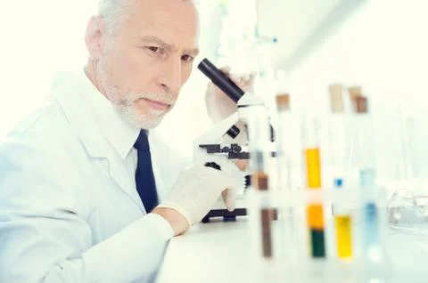 Serious lab worker with microscope looking at test tubes Stock Photos
