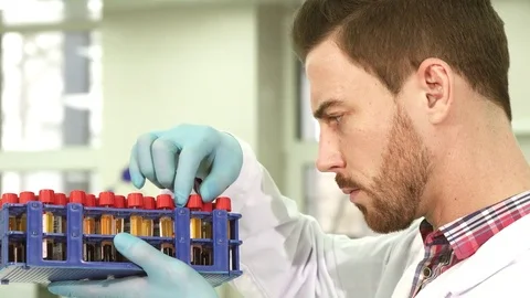 Serious laboratory assistant carefully examines test tubes with assays Stock Footage 84867528