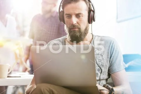 Serious male design professional with headphones using laptop in office Stock Photos
