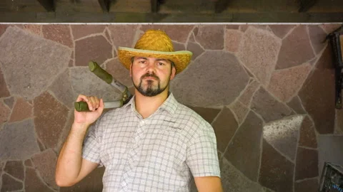 Serious man with a beard and a straw hat is standing against the wall 4K Stock Footage 115550266