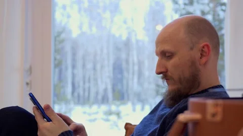 A serious man with a beard sits on the couch, looks attentively at his Stock Footage 172394091