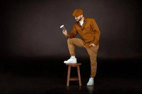 Serious man in beige hat standing on chair with one leg Stock Photos