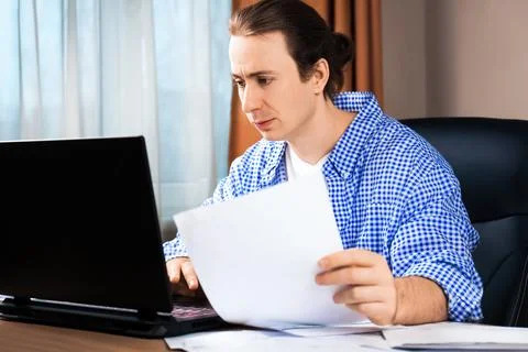 Serious man checking documents while working on a laptop. Concept of remote.. Stock Photos