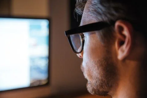 Serious man in glasses using computer and looking at screen 스톡 사진