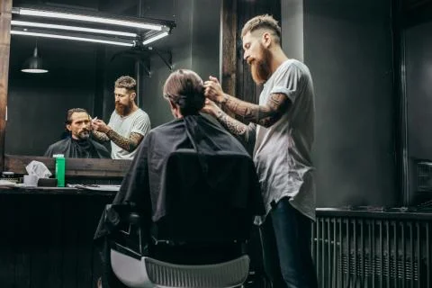 Serious man looking at his reflection while barber working Stock Photos