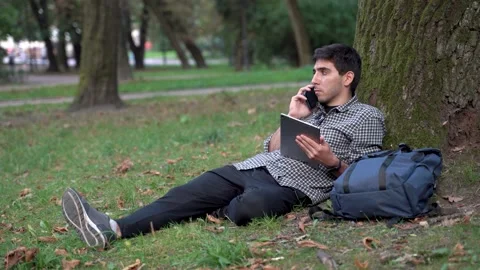 Serious man lying on the grass under tree in the city park Stock Footage 197437125