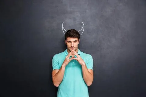 Serious man playing role of devil standing over blackboard background Stock Photos