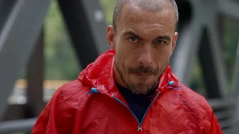 Serious man is putting on head red hood and kneading hands, looking at camera Vídeo Stock 163329323