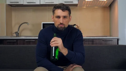 Serious man sitting on the couch, drinking beer and gets angry, swears on a TV Stock Footage 121840815