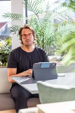 A serious man is sitting at a table working with his tablet, vertical photo Foto stock