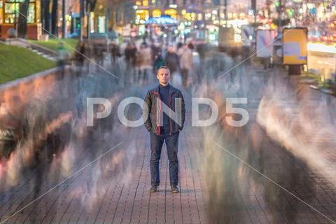 The serious man stand in the ghost-like crowd stream. Evening - night time,.. Stock Photos