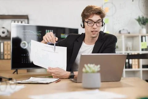 Serious man in suit talking to client on video call, presenting paper graphic Stock Photos