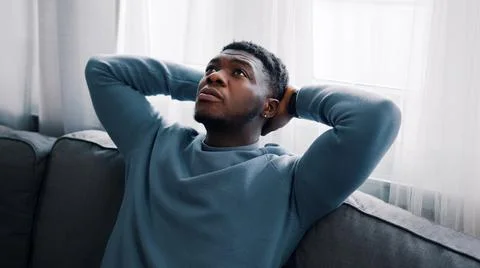 Serious man thinking while sitting on a blue sofa Hands behind the head and Stock Photos