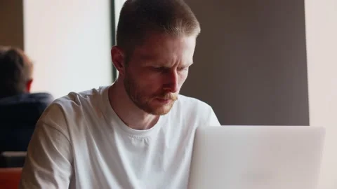 A serious man is typing on the keyboard of his laptop while sitting in a cafe Stock Footage 236643790