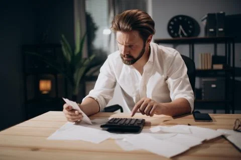 Serious man using calculator for rechecking bills at office Stock-Fotos