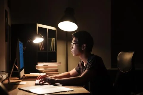 Serious man using computer and typing in dark room 库存照片