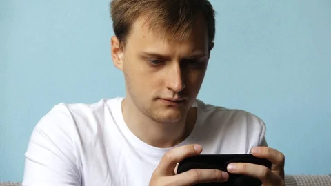 Serious man using a smartphone playing games or typing a message, sitting on  Stock Footage 107664906