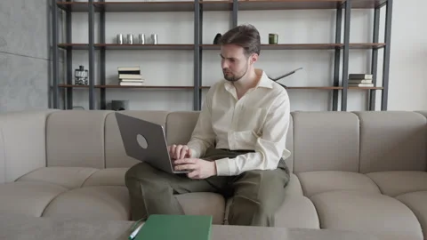 Serious Man Working On Laptop Placed On His Lap Sitting Comfortably On Sofa 스톡 동영상 303759002