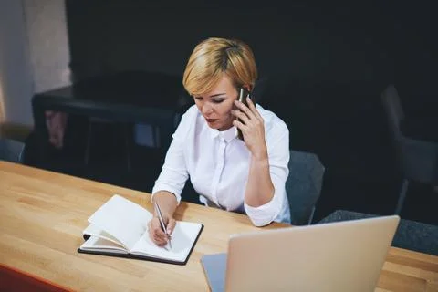 Serious manager writing on notebook while talking on smartphone in office Stock Photos