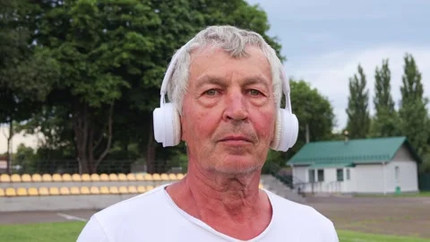 Serious mature gray haired man in wireless headphones doing warming up before Stockbeeldmateriaal 291322327